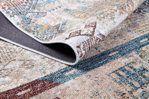 Load image 1 in gallery view. A close-up of the Global Glamour - Washable Rug (JR1708) with geometric blue, brown, cream, and beige patterns shows its corner lifted to display a dark textured backing—perfect for easy care and machine washing.