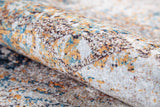A close-up of the Global Glamour - Washable Rug - JR1708, showcasing its soft, plush texture and abstract cream and beige pattern with blue, orange, brown, and white accents—perfect for stylish spaces seeking easy-care rugs.