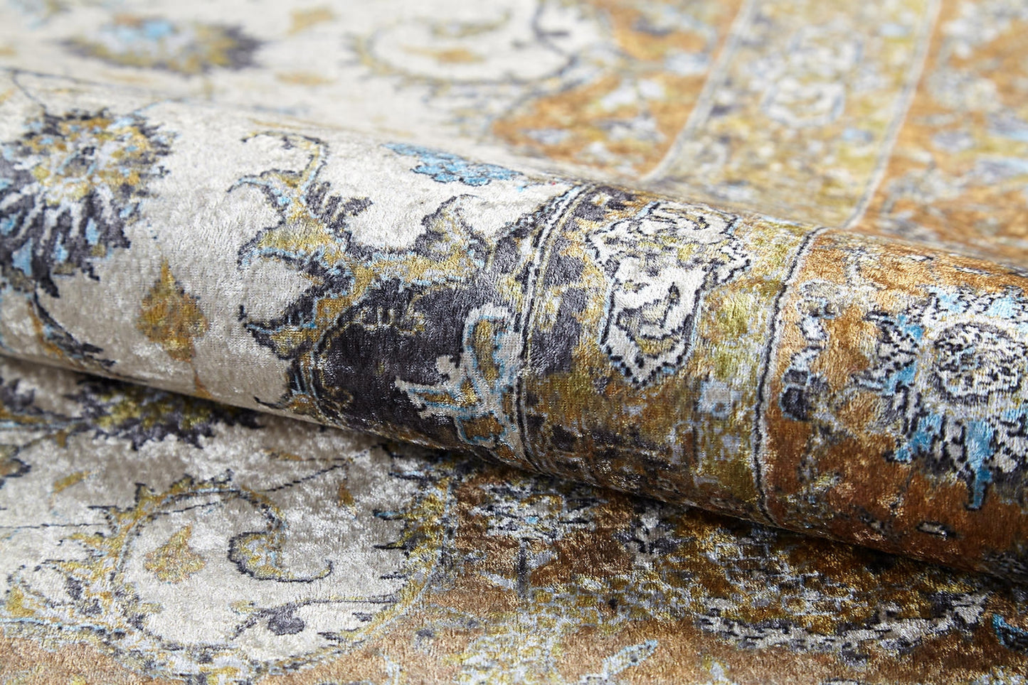 Close-up of the Golden Oasis - Washable Rug (JR1930), rolled up to reveal intricate floral and paisley patterns in gold, blue, black, and cream—durable, washable, and ideal for high-traffic areas with its textured, vintage look.