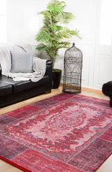 A living room with a black leather sofa, gray blanket and pillow, potted plant, large birdcage, and the Golden Wonder - Washable Rug - JR306 in red—perfect for high-traffic areas—on a light wooden floor.