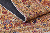 A close-up of the Grandiose Grace - Washable Rug - JR44 shows its multicolored geometric patterns in red, gold, blue, and brown. A folded corner reveals the dark underside—ideal for high-traffic areas.