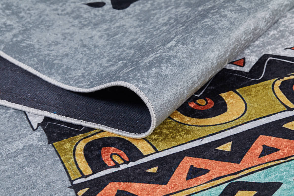 A close-up of the Groovy Bear - Machine-Washable Rug JRC093 in gray-anthracite shows a folded edge and bold geometric shapes in yellow, orange, black, and teal—ideal for adding style to high-traffic areas.