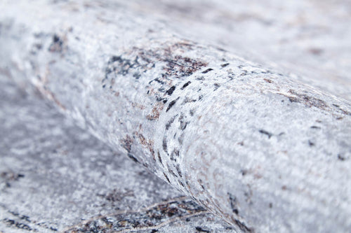Load image 1 in gallery view. A close-up of the Heritage Jewel - Washable Rug - JR1778 showcases its textured, light gray surface with mottled, stone-like patterns in darker shades, reminiscent of a flat weave rug.