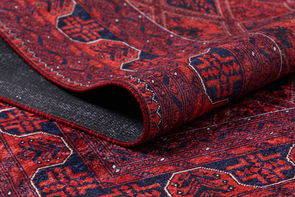 A close-up of the Imperial Impressions - Washable Rug - JR1132 shows its red and navy geometric pattern. The curled edge reveals the dark underside and texture, making this rug ideal for high-traffic areas.