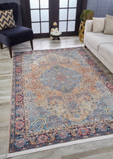 The Imperial Weave - Washable Rug - JR1969, featuring blue, red, and tan intricate patterns, rests on a wooden floor between a cream sofa and dark armchair—ideal for modern living rooms with large windows and high-traffic areas.