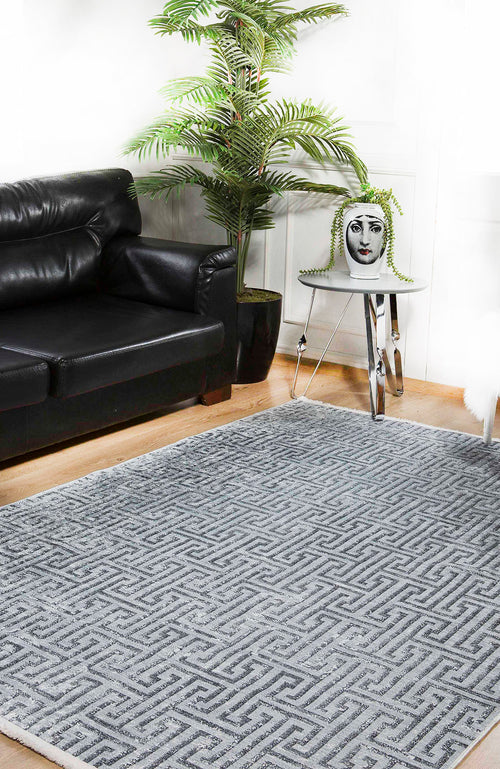 Bild 1 in Galerieansicht laden. A modern living room with a black leather sofa, large potted plant, metallic side table with a face-printed vase, and the Jazz Age - Washable Rug - JR1225 in gray-anthracite—ideal for high-traffic areas—on a wooden floor.