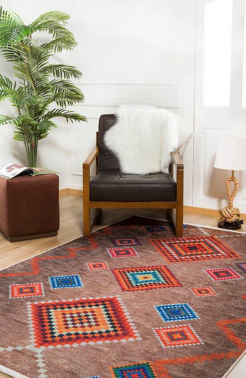 Load image 1 in gallery view. A cozy reading nook with a brown armchair draped in a white faux fur throw, the Kilim Kingdom Washable Rug (JR1536), a small ottoman holding a magazine, a potted plant, and a table lamp on light wooden floors.