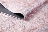 A close-up of the Luxurious Design - Washable Rug - JR1924 in soft pink, with a folded corner showing its textured black underside and faded beige and brown patterns—ideal for adding style to busy spaces.