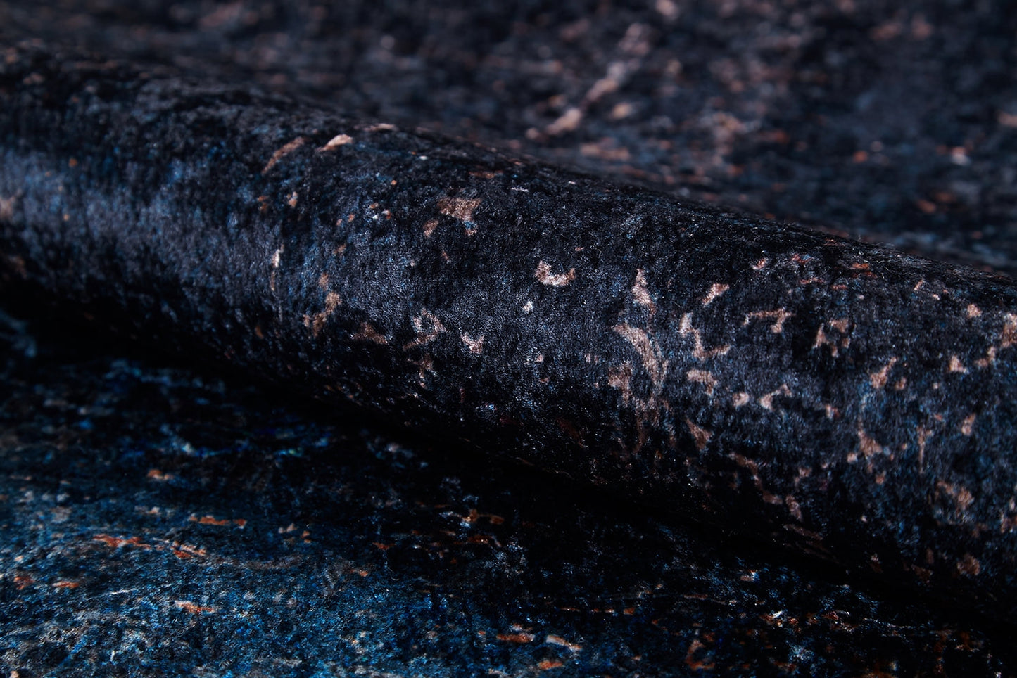 A close-up of the Luxurious Fleur - Washable Rug (JR1897) reveals a dark, textured surface with blue and brown shades, a rolled edge, subtle sheen, and speckled look—ideal for high-traffic areas.