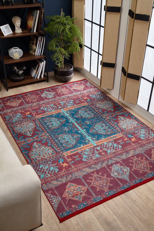 Load image 1 in gallery view. The Majestic Mandarin - Washable Rug (JR1863), with vibrant red patterns, decorates a modern living room featuring wooden floors, a beige sofa, tall windows with bamboo shades, and a cozy reading nook—durable and easy to clean.