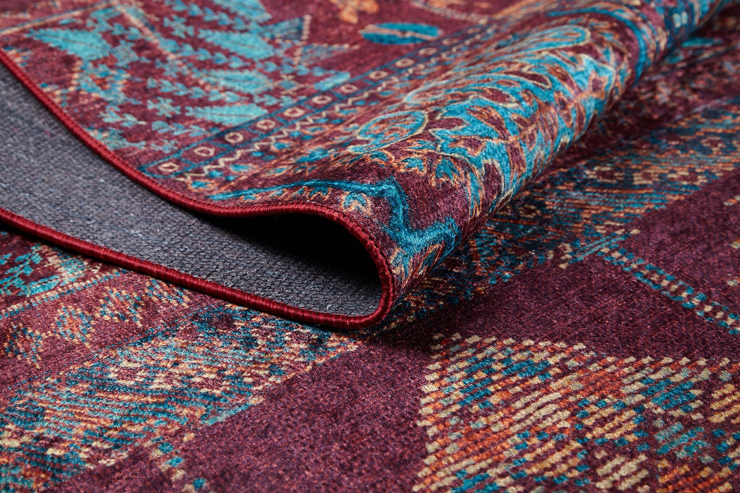 A close-up of the Majestic Mandarin - Washable Rug - JR1863, featuring folded, intricate geometric and floral designs in blue, yellow, and teal on a maroon background—its visible texture makes it ideal for high-traffic areas or stylish décor.
