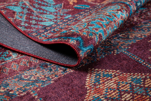 Load image 1 in gallery view. A close-up of the Majestic Mandarin - Washable Rug - JR1863, featuring folded, intricate geometric and floral designs in blue, yellow, and teal on a maroon background—its visible texture makes it ideal for high-traffic areas or stylish décor.