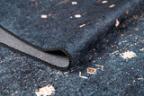 A close-up of the Midnight Majesty - Machine-Washable Rug (JRS5052) in blue, featuring textured fabric with small geometric white and orange patterns and a folded edge revealing the backing—ideal for high-traffic areas.