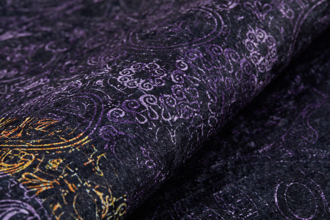 A close-up of the Minimalist and Elegant - Washable Rug - JR1298 shows a dark, textured surface with purple swirling patterns and gold accents, offering an ornate design that's decorative and ideal for high-traffic areas.