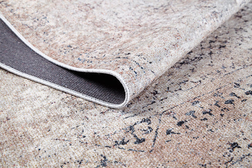 Load image 1 in gallery view. A close-up of the Misty Mosaic - Washable Rug (JR1690) in beige and gray shows a partially folded corner that reveals its dark, textured backing. The rug features a subtle, distressed mosaic pattern with hints of black markings.