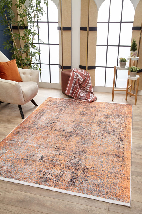 Load image 1 in gallery view. A living room with large grid windows, the Modern Mosaic - Machine-Washable Rug JR1846 in orange and gray for high-traffic areas, a beige armchair with orange pillows, brown ottoman with striped blanket, potted plants, and wood flooring.