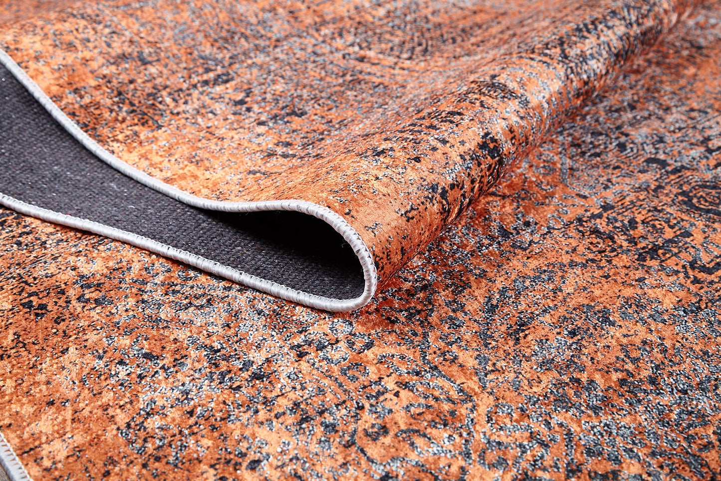 A close-up of the Modern Mosaic - Machine-Washable Rug JR1846 shows its textured orange and black pattern, a folded corner revealing its plain dark underside and stitched edge—perfect for high-traffic spaces.