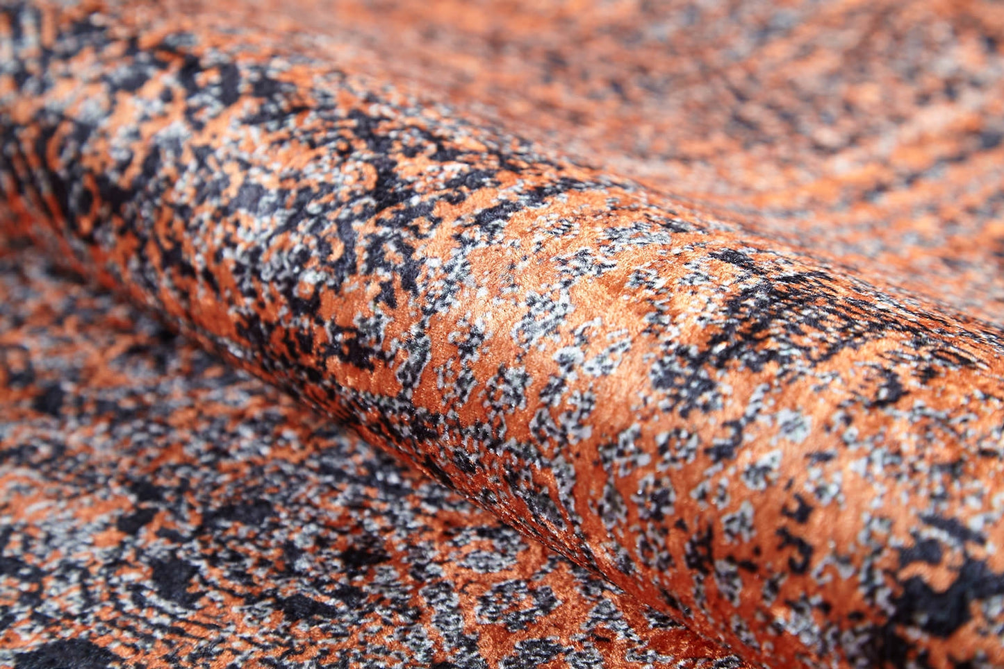 A close-up of the Modern Mosaic - Machine-Washable Rug JR1846 reveals its orange and black pattern, detailed texture, and intricate mottled design. The gently folded material highlights this rug’s softness and durability for high-traffic areas.