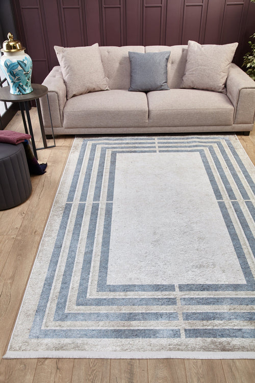 Load image 1 in gallery view. A modern living room with a light beige sofa, three cushions, a decorative vase on a side table, and the Modern and Regal - Washable Rug - JR1616 showcasing blue and gray rectangles on the wooden floor.