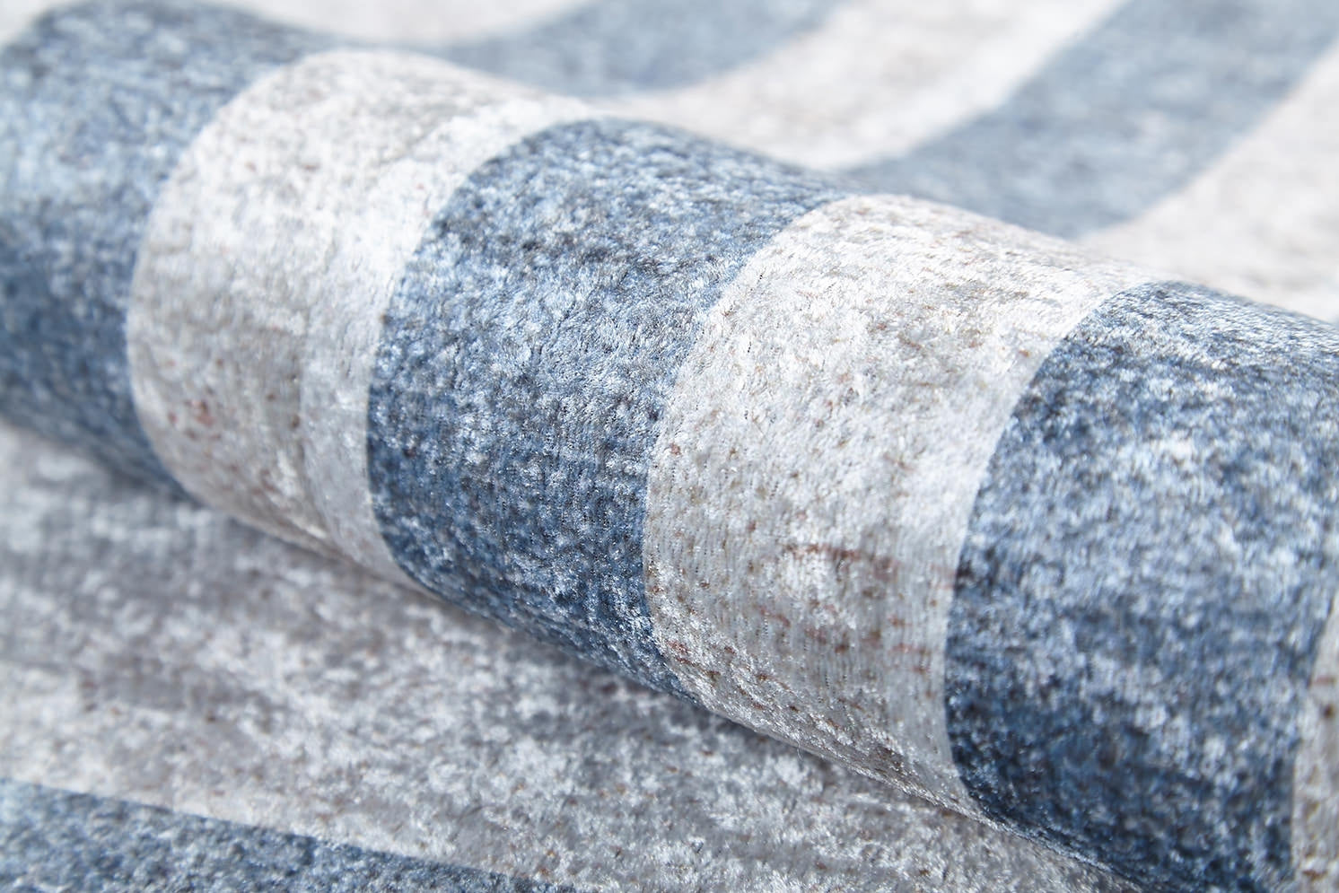 Close-up of the Modern and Regal - Washable Rug - JR1616, shown rolled up with alternating blue and light gray horizontal stripes in a textured flat weave style.