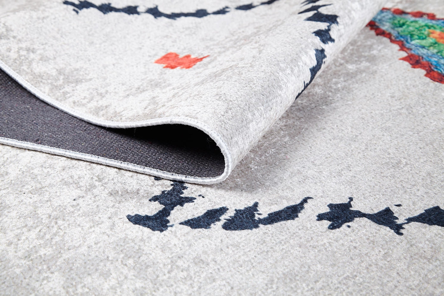 A close-up of the Moroccan Mosaic - Washable Rug - JR1655 displays abstract black, red, and multicolored patterns, ideal for high-traffic areas, with one corner lifted to reveal its dark backing.