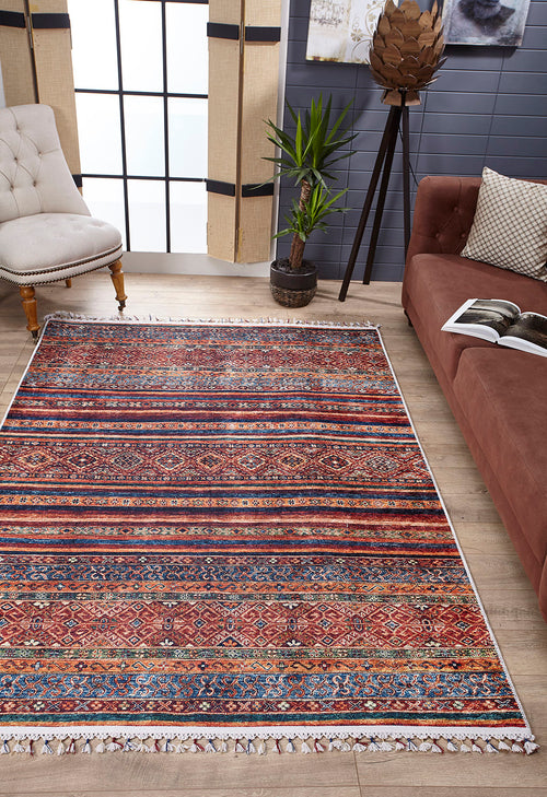 Load image 1 in gallery view. A living room featuring the Native Nightscape - Washable Rug - JR5093, ideal for high-traffic areas, a brown sofa with an open book, a potted plant, a tufted beige chair, large windows with natural light, and light wood floors.