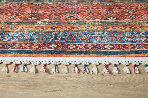 Load image 1 in gallery view. A close-up of the Native Nightscape - Washable Rug - JR5093, showcasing multicolor geometric patterns in blue and red, with white fringes accented by red and blue threads, resting on a light wood floor—ideal for high-traffic areas.