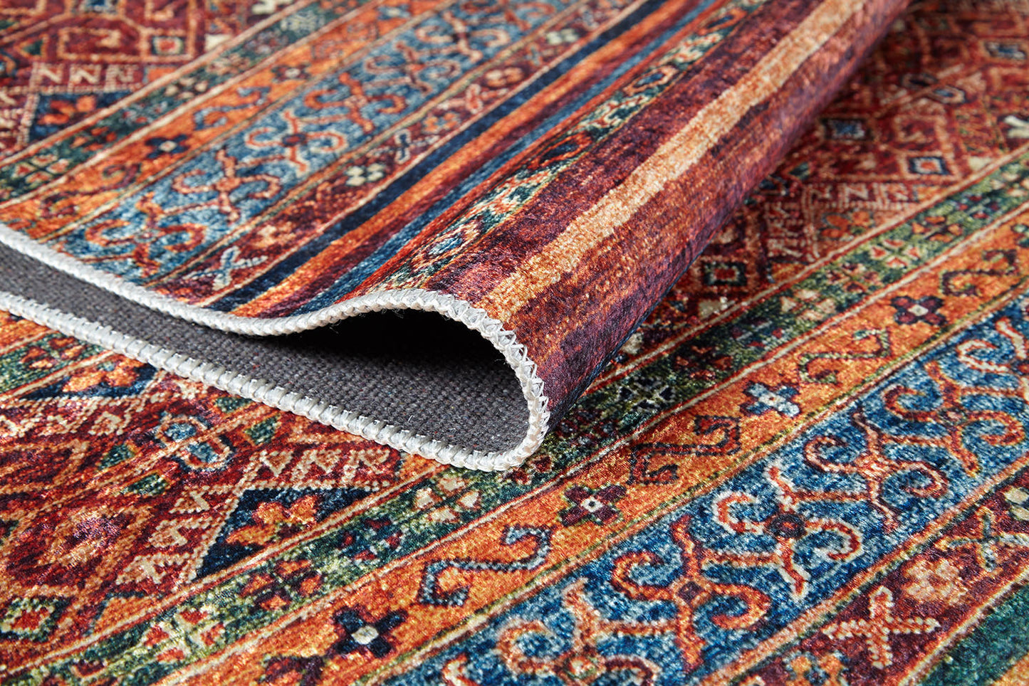 A close-up of the Native Nightscape - Washable Rug - JR5093, featuring intricate multicolor geometric and floral designs in orange, blue, red, and green. One folded corner reveals its washable underside—ideal for high-traffic areas.