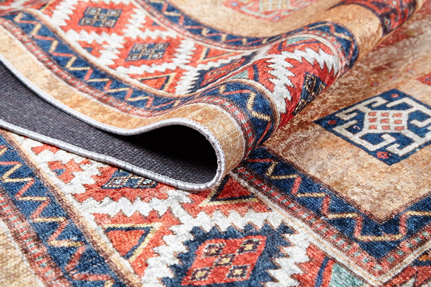 A close-up of the Navajo Nights - Washable Rug (JR1758) featuring vibrant geometric and diamond patterns in red, blue, orange, and beige. One corner is curled up to show the dark backing—perfect for high-traffic areas.