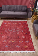 A modern living room with a grey sofa, round wooden side table with a plant, and the Nomadic Journey - Washable Rug - JR5080, featuring geometric red designs on light wood floors. Red vertical wall paneling completes this high-traffic area.