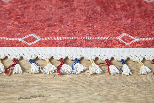Load image 1 in gallery view. Close-up of the Nomadic Journey - Washable Rug - JR5080: a red rug with white geometric edge designs, white fringe with red and blue threads. Washable and perfect for high-traffic areas, it complements wooden floors beautifully.