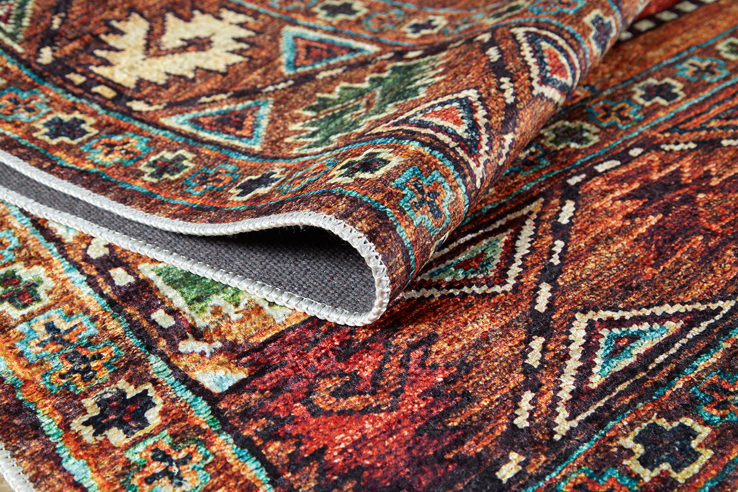 A close-up of the Nomadic Oasis - Washable Rug - JR5086 shows its colorful geometric designs in red, orange, green, and blue. The folded corner highlights the woven texture and intricate details typical of this high-quality washable rug.