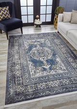 A room with the Opulent Beauty - Washable Rug - JR1932 in blue and white on a wooden floor, a dark armchair, beige sofa, decorative vase, and French doors with frosted glass panels in the background—ideal for high-traffic areas.