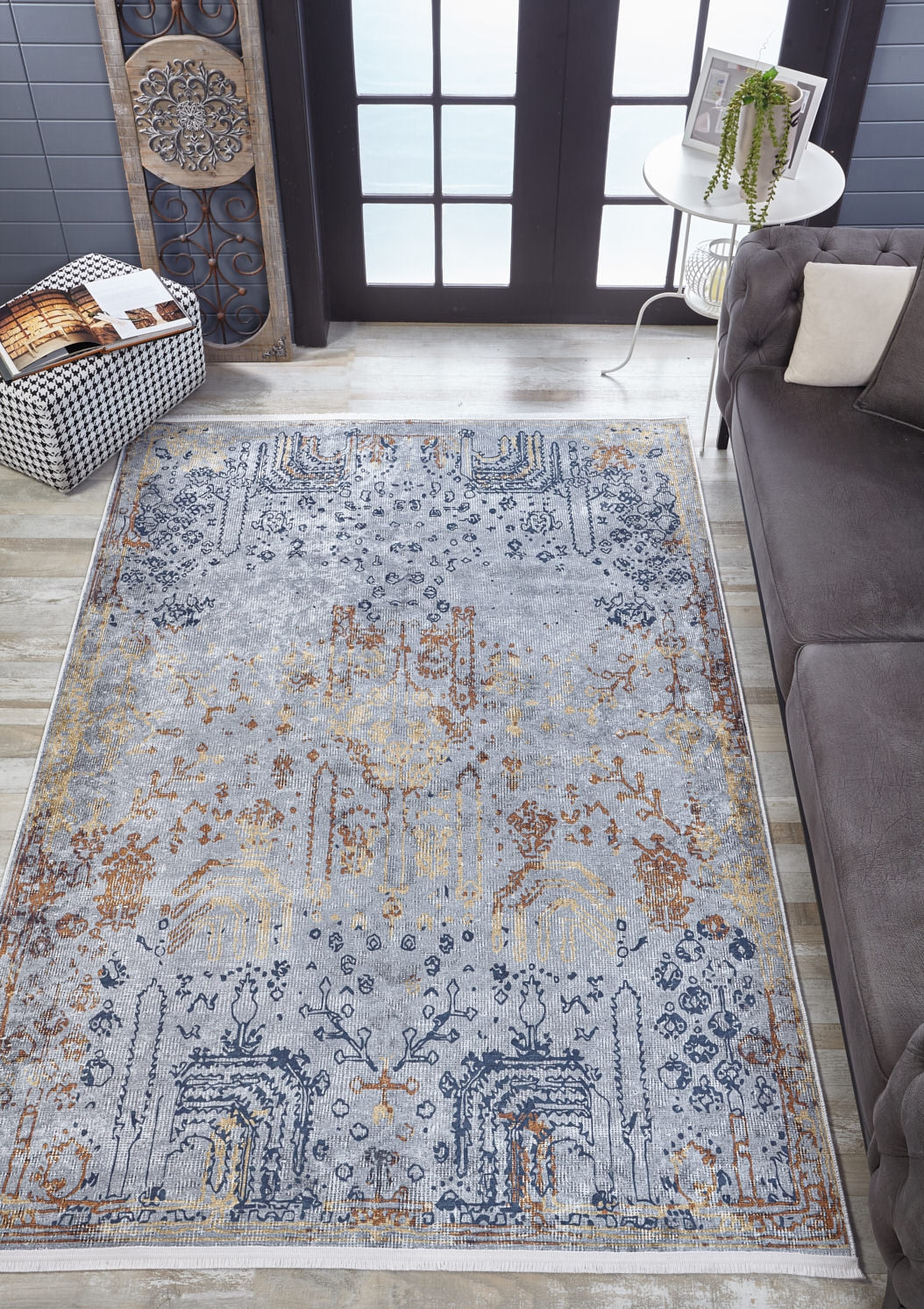 The Oriental Treasures - Machine-Washable Rug JR1613, featuring blue, gold, and beige patterns, lies on a wooden floor by a gray sofa and a white table with a plant—ideal for allergy-sensitive or high-traffic areas.
