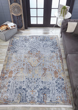 The Oriental Treasures - Machine-Washable Rug JR1613, featuring blue, gold, and beige patterns, lies on a wooden floor by a gray sofa and a white table with a plant—ideal for allergy-sensitive or high-traffic areas.