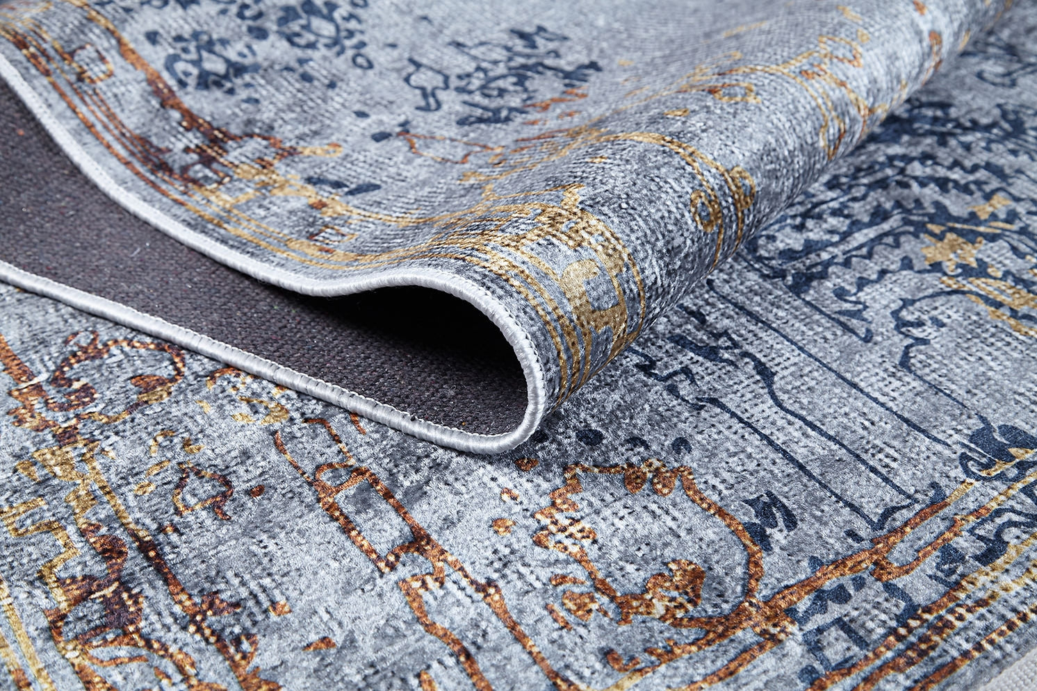 A close-up of the Oriental Treasures - Machine-Washable Rug JR1613 in gray, blue, and gold, with a folded corner showing its texture and underside—an ideal choice for high-traffic spaces.