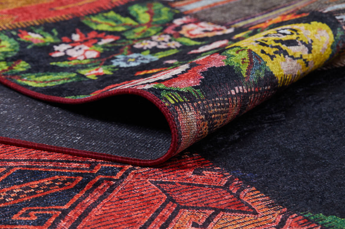 A close-up of the Petal Paradise - Washable Rug - JR315, with a corner slightly folded over to reveal intricate floral and geometric patterns in red, black, green, yellow, and white—ideal for high-traffic areas.
