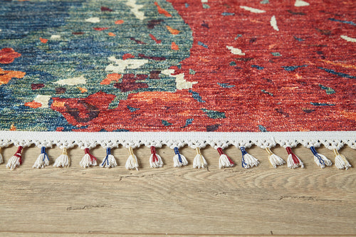 Load image 1 in gallery view. The Psychedelic Splash - Machine-Washable Rug (JR5096), featuring vibrant red, blue, and green patterns with white fringe and colorful tassels, lies on a wooden floor—ideal for high-traffic areas.