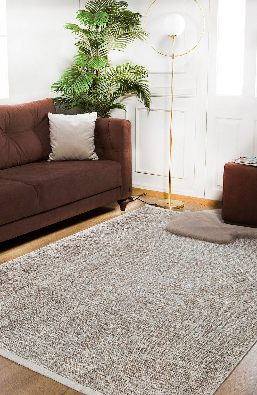A modern living room with a brown sofa, beige pillow, Pure Bliss - Washable Rug - JR745 (Outlet) US for high-traffic areas, potted plant, floor lamp with round shade, and white walls with windows.