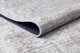 A close-up of the Pure Bliss - Washable Rug - JR745 (Outlet) US shows its cream and beige finish with subtle beige and gray speckles. A folded corner reveals the dark underside and detailed stitching, making it perfect for high-traffic areas.