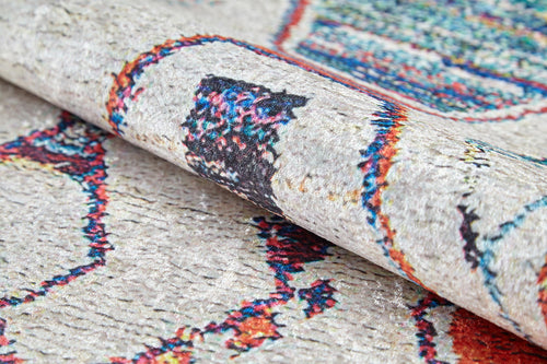 Load image 1 in gallery view. A close-up of the Rainbow Rhapsody - Washable Rug (JR5060), featuring a rolled, textured flat weave with bold, colorful abstract shapes and lines on a light background.