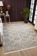 The Regal Embellishment - Washable Rug - JR1590, a light flat weave with intricate floral patterns, decorates the wooden floor beside a white sofa, plant in a pot, small table with vase, and dark paneled walls with tall windows.