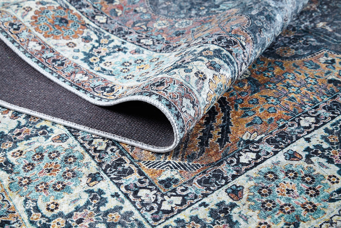 A close-up of the Royal Sultan - Washable Rug - JR1970 showcases its intricate blue, orange, and cream floral-geometric patterns. One corner is folded to reveal the textured underside—perfect for allergy-sensitive homes.