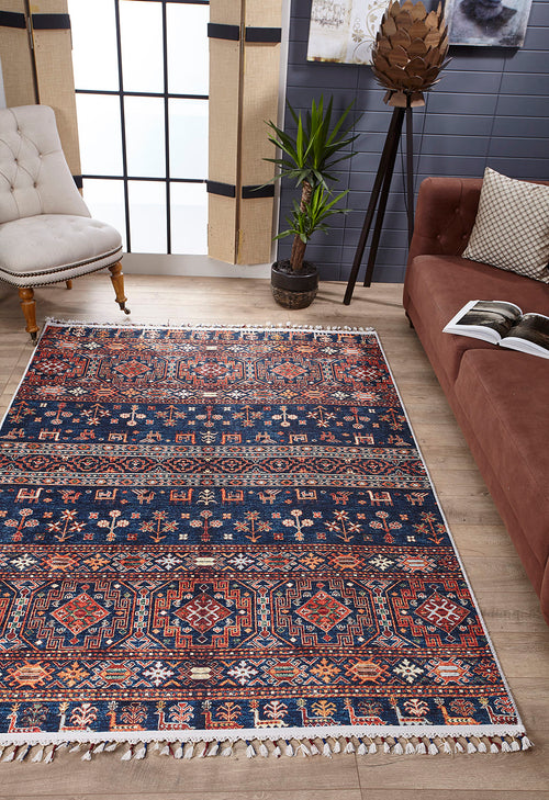 Load image 1 in gallery view. A living room featuring the Sahara Sunrise - Washable Rug - JR5091, ideal for high-traffic areas, a brown couch with an open book, a beige tufted chair, a potted plant, and large windows letting in natural light.