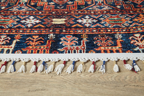 Load image 1 in gallery view. A close-up of the Sahara Sunrise - Washable Rug - JR5091, featuring colorful geometric and floral patterns, white fringe tassels with red and blue accents—ideal for allergy-sensitive or high-traffic areas—on a light wooden floor.