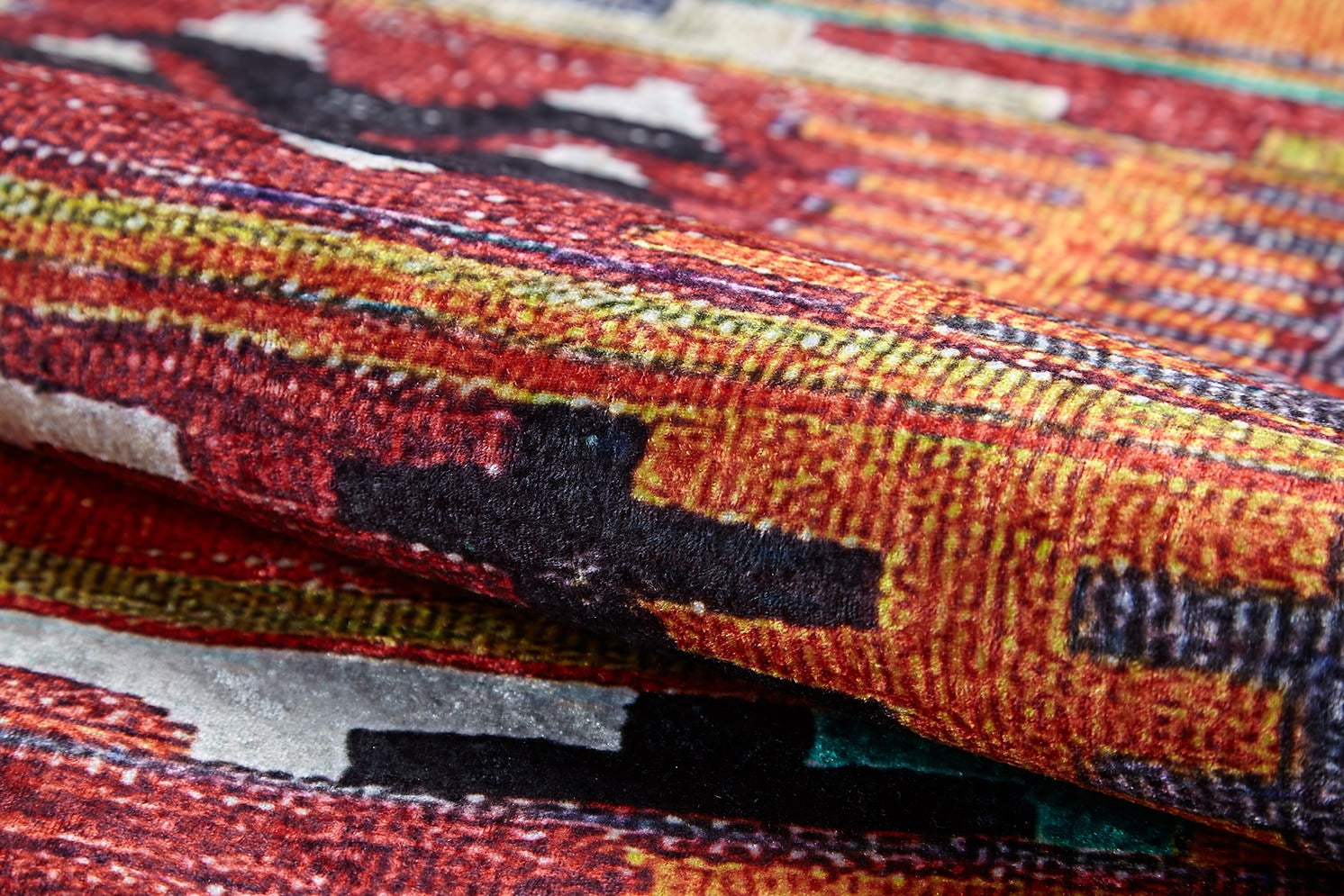 Close-up of the Serene Sahara - Washable Rug - JR1959, featuring bold red, orange, yellow, black, and white geometric patterns. Its folded fabric highlights texture—ideal for high-traffic areas and easy washing.