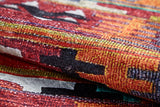 Close-up of the Serene Sahara - Washable Rug - JR1959, featuring bold red, orange, yellow, black, and white geometric patterns. Its folded fabric highlights texture—ideal for high-traffic areas and easy washing.
