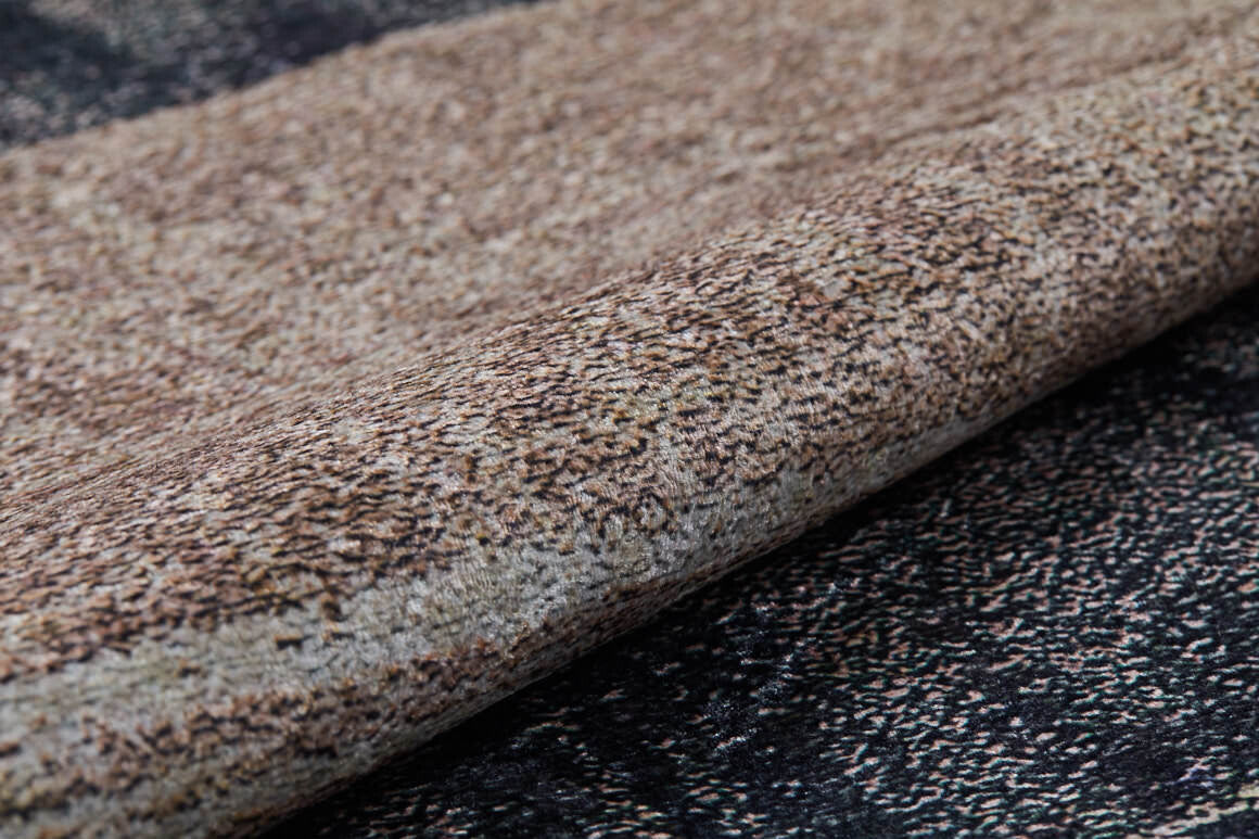 A close-up of the Serene Swirls - Washable Rug - JR952, featuring a speckled bronze and brown pattern, rolled up on a darker, matching surface—ideal for high-traffic areas.