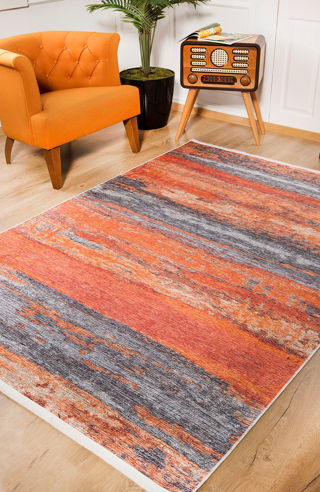 The Sleek Brushed - Washable Rug - JR431 features vibrant orange and gray abstract patterns, brightening wooden floors. Ideal for high-traffic areas, it pairs well with a bold armchair, lush plant, and retro radio for vintage charm.