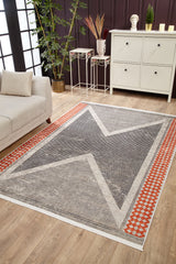 A modern living room with the Sleek Design - Washable Rug - JR1727, featuring a geometric X pattern and orange border—perfect for allergy-sensitive, high-traffic areas—plus a white sofa, cabinet, indoor plants, and wooden flooring.